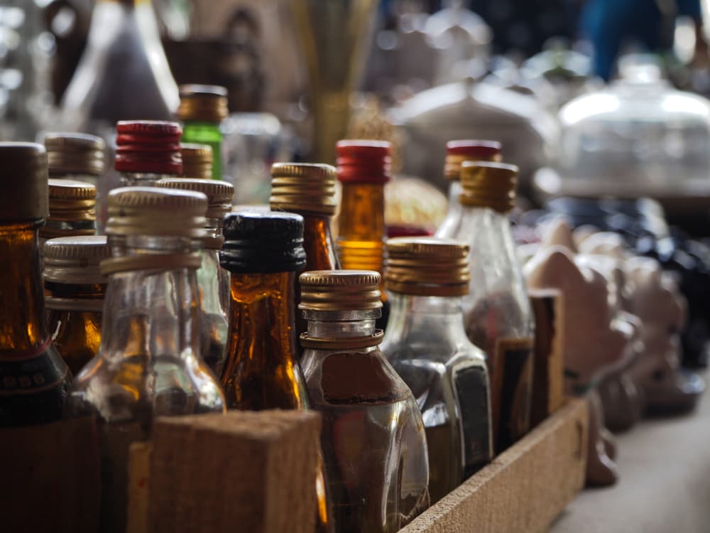 Old, small liquor bottles displayed in a wooden case at an antique market.






