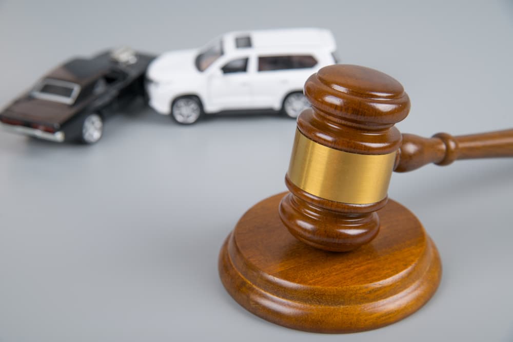 A judge's gavel next to two collided cars on a gray background, symbolizing an accident, insurance, and a court case.