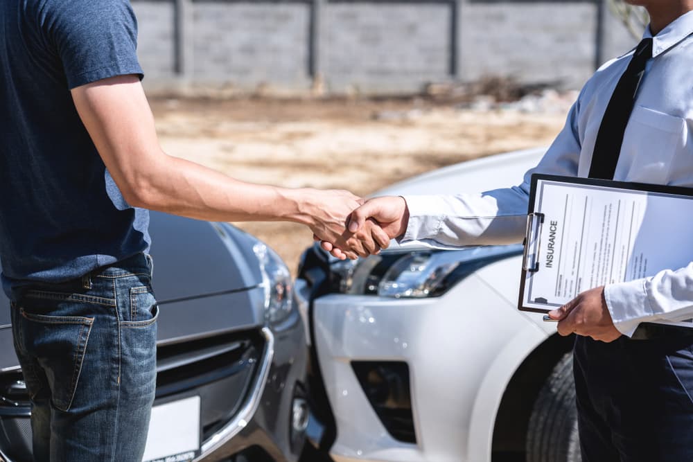 An insurance agent and a customer shaking hands after reaching an agreement on an insurance claim, having assessed the car crash, checked, and signed the report.






