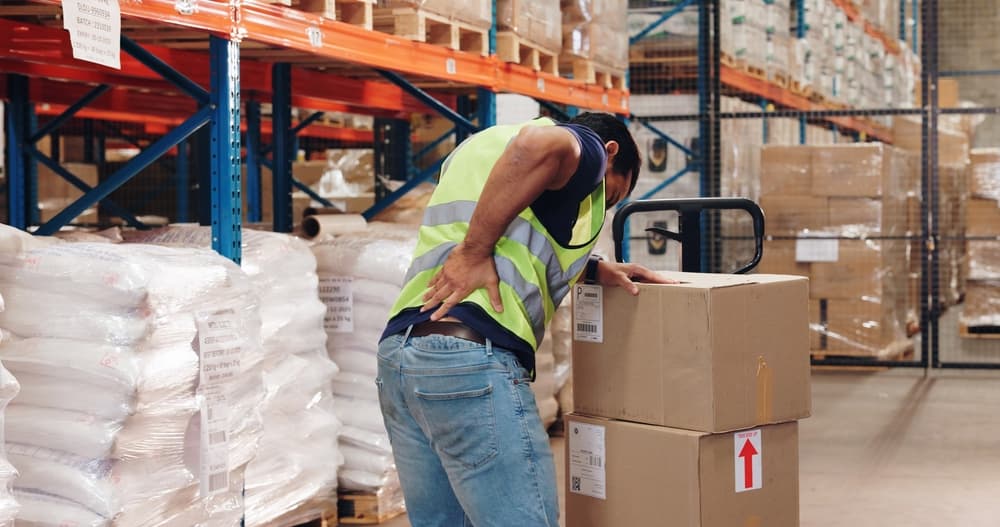 Warehouse worker with a pallet truck experiencing back pain while handling transport, ensuring safety, and managing storage for distribution or delivery.