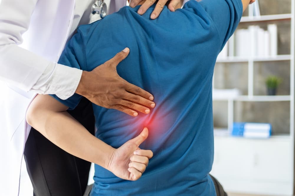 A doctor is diagnosing a male patient’s back pain in a hospital examination room. The patient seeks treatment for his back discomfort.