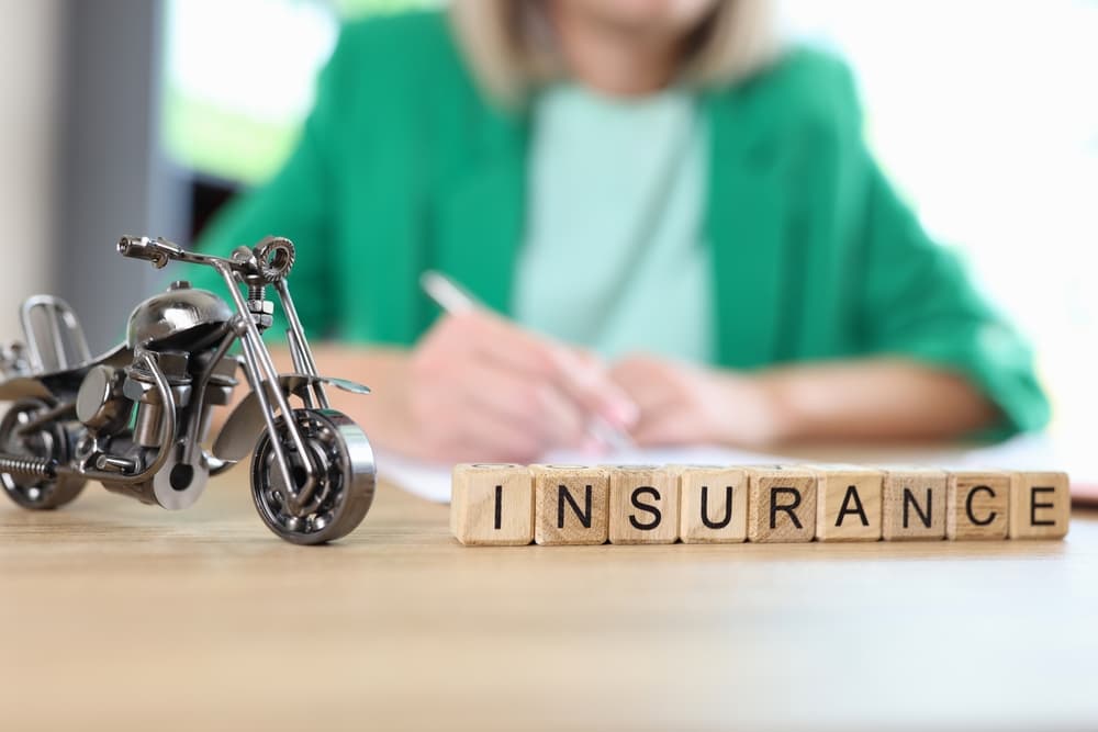 Motorcycle insurance concept featuring a motorcycle model and the word "insurance" on a table, with a blurred manager handling documents in the background.