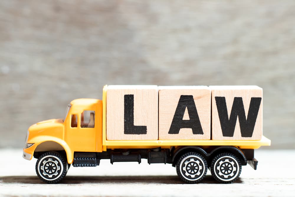 A toy truck holding a letter block forming the word "LAW" on a wooden background.






