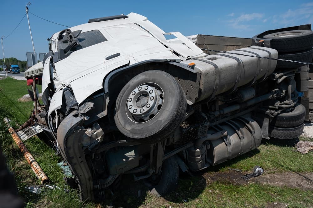 A truck overturned on its side following an accident on the highway. The large vehicle is sprawled across multiple lanes, with debris scattered around.