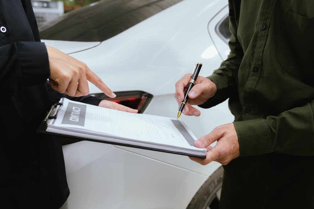 An insurance agent reviews a car accident claim while holding a clipboard, as the customer signs the necessary forms.