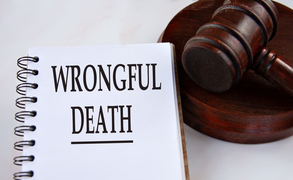 WRONGFUL DEATH written in a white notebook, set against the backdrop of a judge's gavel, symbolizing legal proceedings.