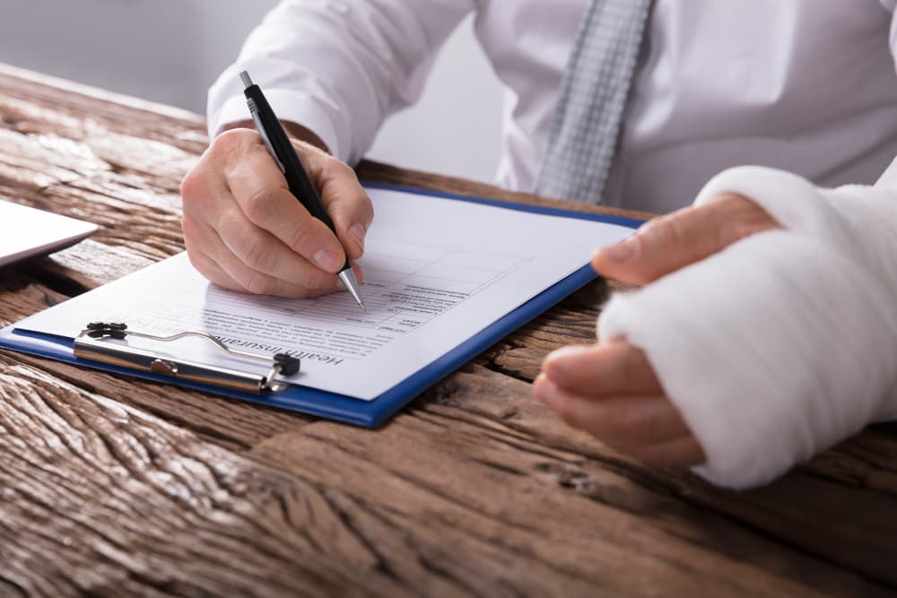 Injured worker with bandaged arm fills out insurance form, highlighting pre-existing condition concerns.