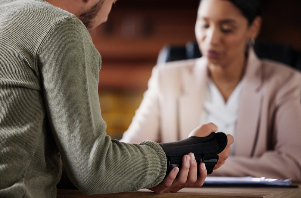 Injured man with a wrist brace discussing his case with a female attorney at a desk.